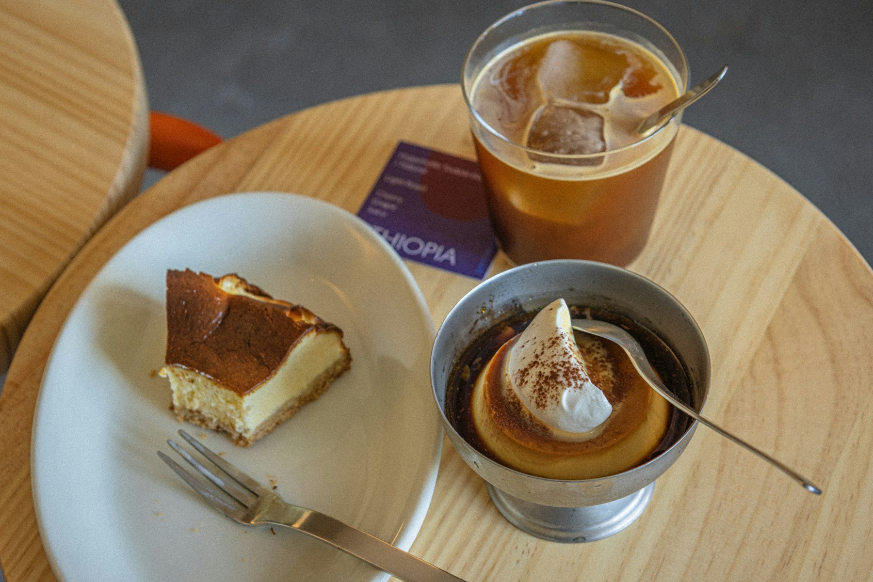 丸いテーブルに置かれたチーズケーキとプリンとアイスコーヒー